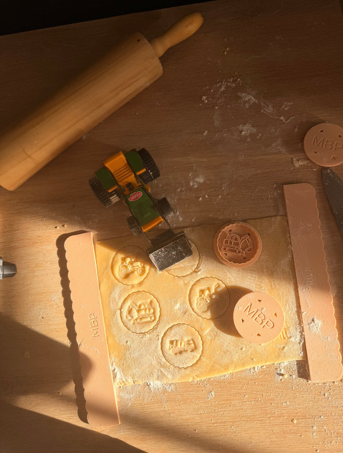 Biscuits sablés imprimés tracteur, tractopelle et camion toupie avec les emporte-pièces Mon Biscuit Perso, sur un plan de travail fariné avec rouleau et tracteur jouet